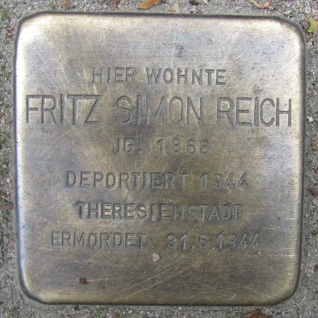 Das Bild zeigt einen verlegten Stolperstein mit der Inschrift: "Hier wohnte Fritz Simon Reich. Jahrgang 1868. Deportiert 1944 nach Theresienstadt. Ermordet am 31.5.1944".