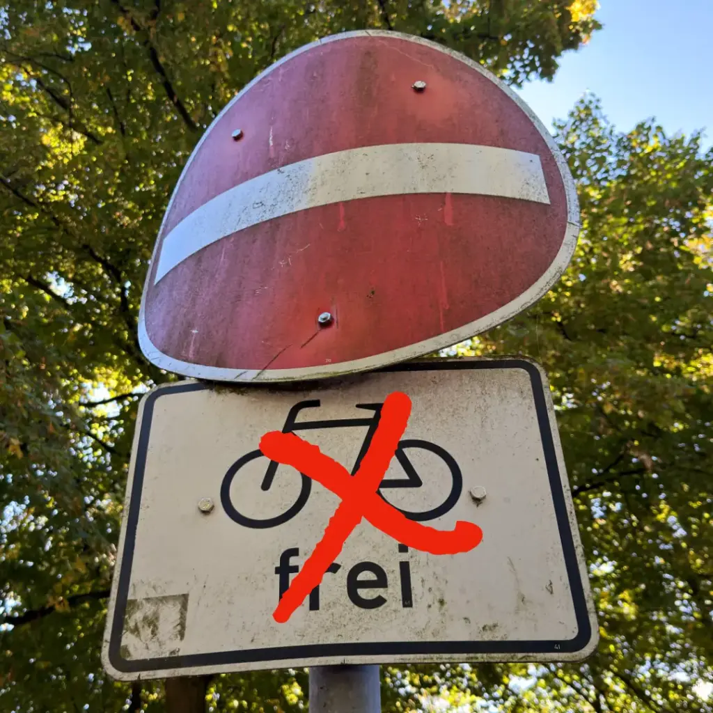 Das Bild zeigt ein Verkehrszeichen "Einfahrt verboten" mit einem Zusatzschild "Fahrräder frei", das mit einem roten Kreuz durchgestrichen ist.